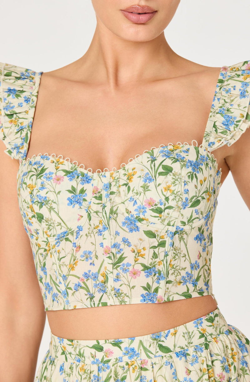Woman in a floral crop top with ruffled shoulder straps and a front zipper.