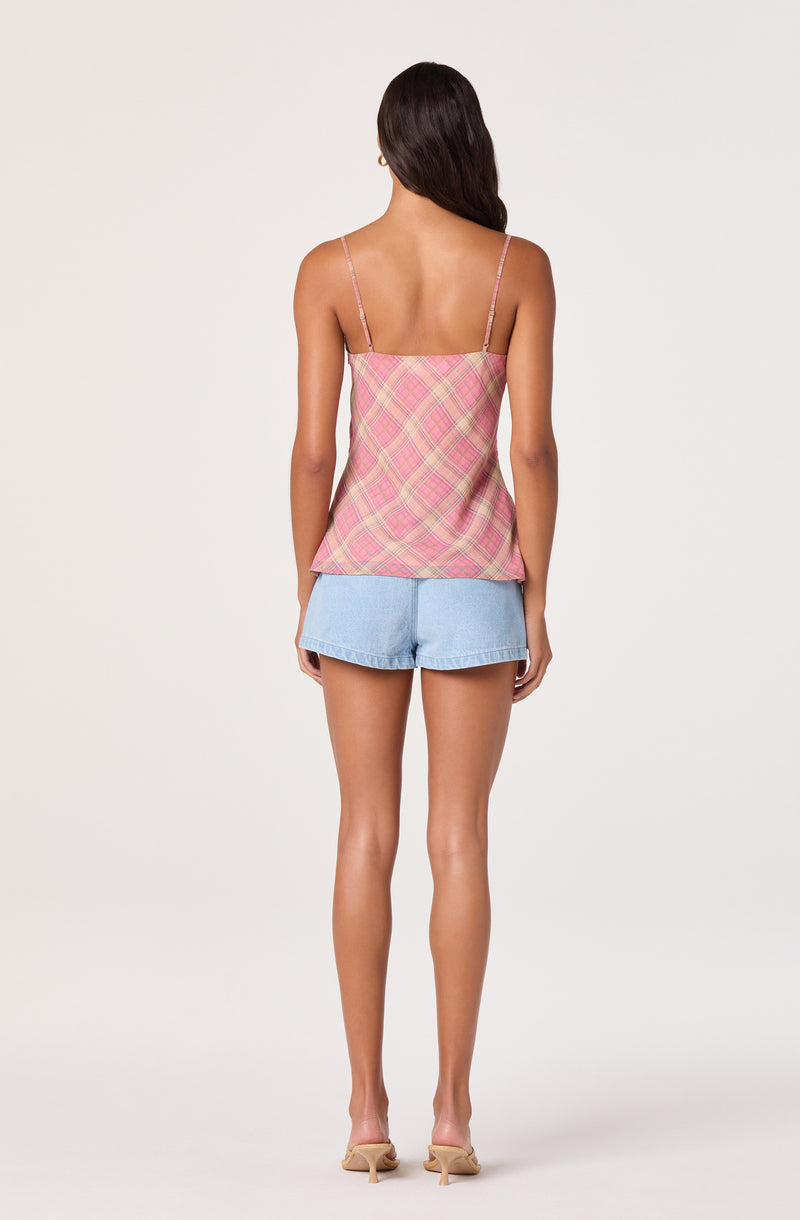 Woman wearing a pink plaid sleeveless top with thin straps and light blue denim shorts.