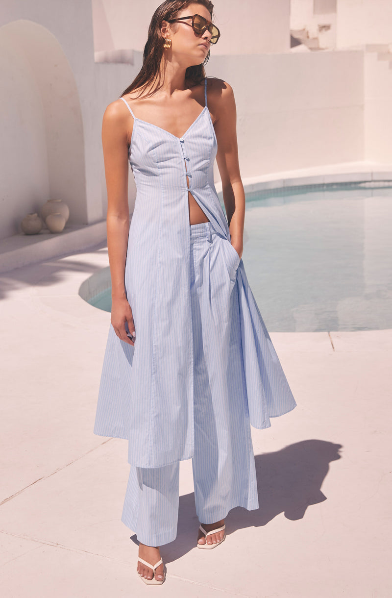 Woman wearing a light blue striped spaghetti strap dress with button details, paired with matching wide-leg pants.