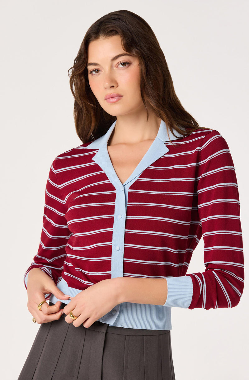 Woman wearing a red cardigan with white stripes and light blue trim.