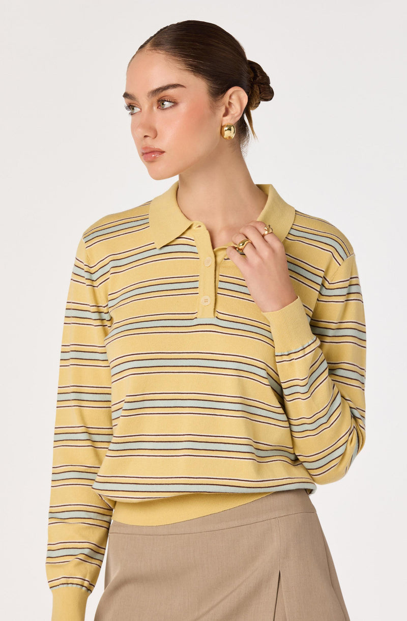 Woman in yellow striped polo shirt and beige skirt, wearing gold earrings and rings.