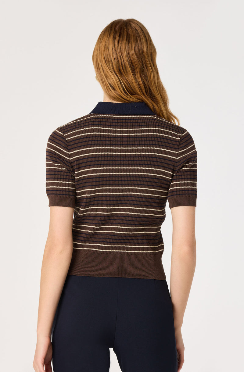 Woman wearing a short-sleeve brown striped sweater with a navy collar, and dark pants.