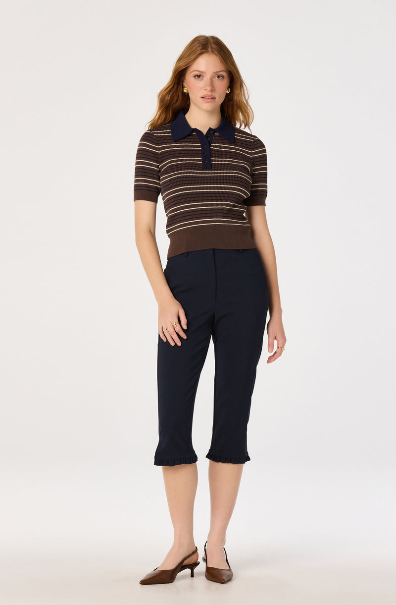 Woman wearing a short-sleeve, striped brown and navy polo shirt with a navy collar and buttons, and navy cropped pants with ruffled cuffs.