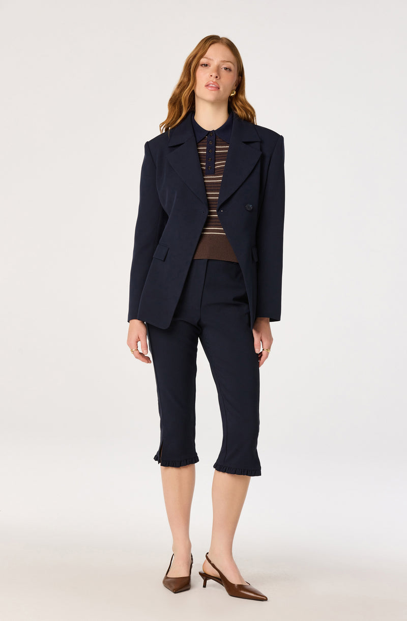 Woman wearing a dark navy blazer, striped top, cropped navy pants, and brown heels.