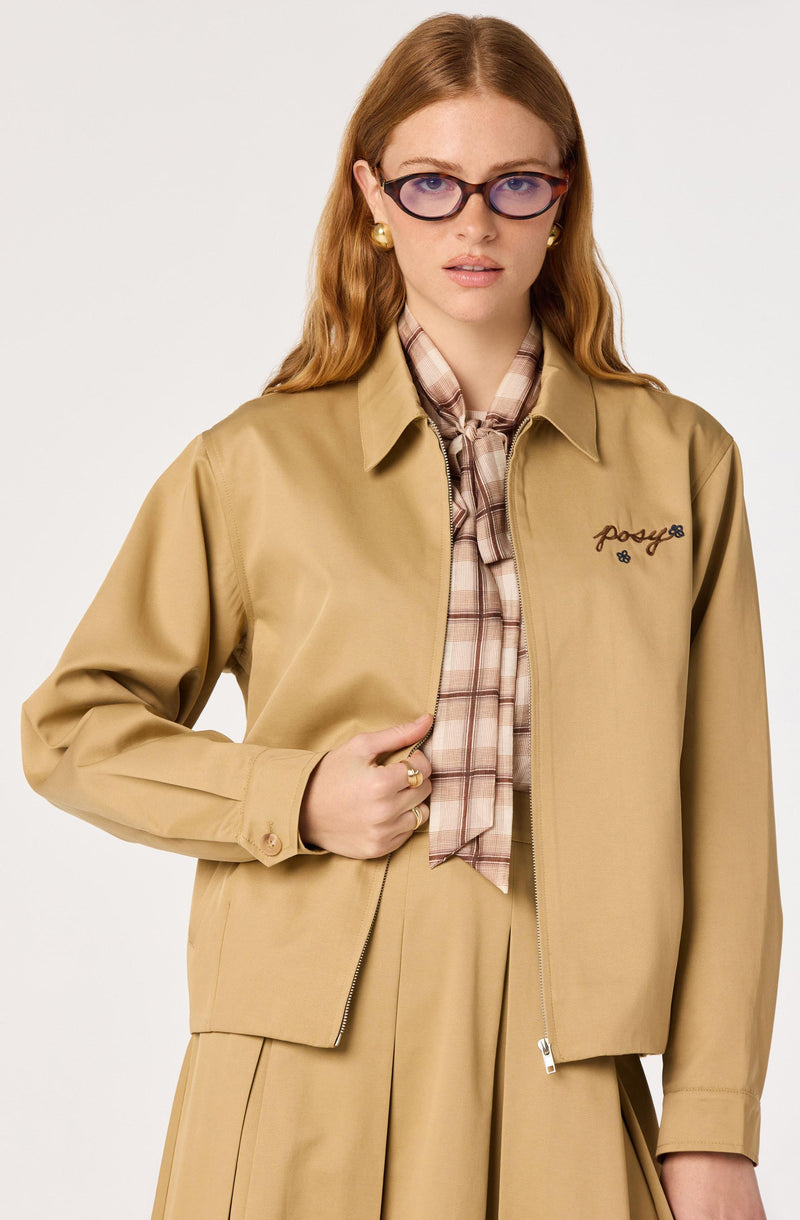 Woman wearing a beige jacket over a plaid shirt, with a matching beige skirt.