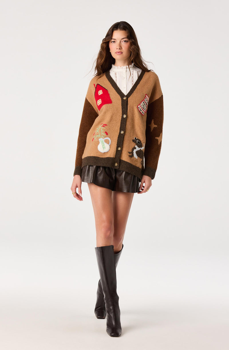 Girl wearing a colorful, patterned cardigan with patches, a white blouse, a black leather skirt, and tall black boots.