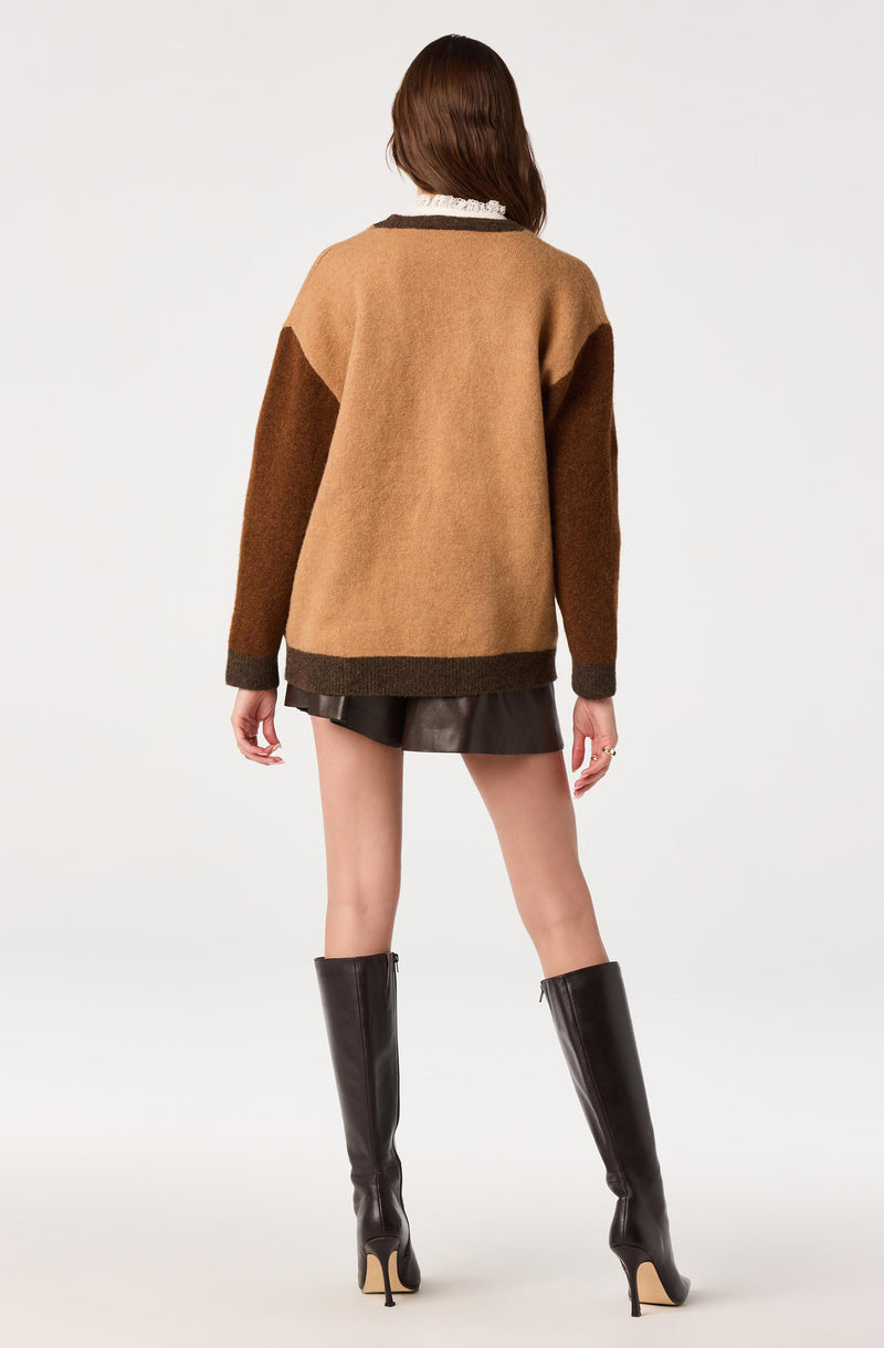 Woman in color-blocked oversized sweater with black leather shorts and tall black heeled boots.