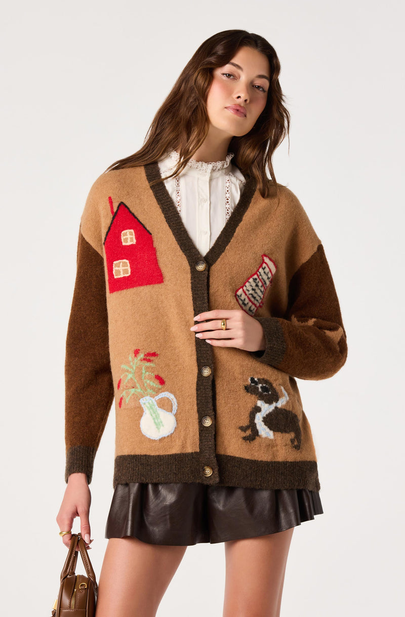 Model wearing a large brown and tan cardigan with embroidered house, dog, potted plant, and hat.