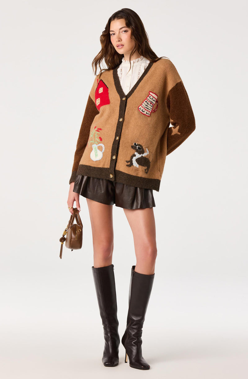 Oversized cardigan with colorful patches, layered over a white lace blouse, paired with black leather shorts and knee-high black boots.