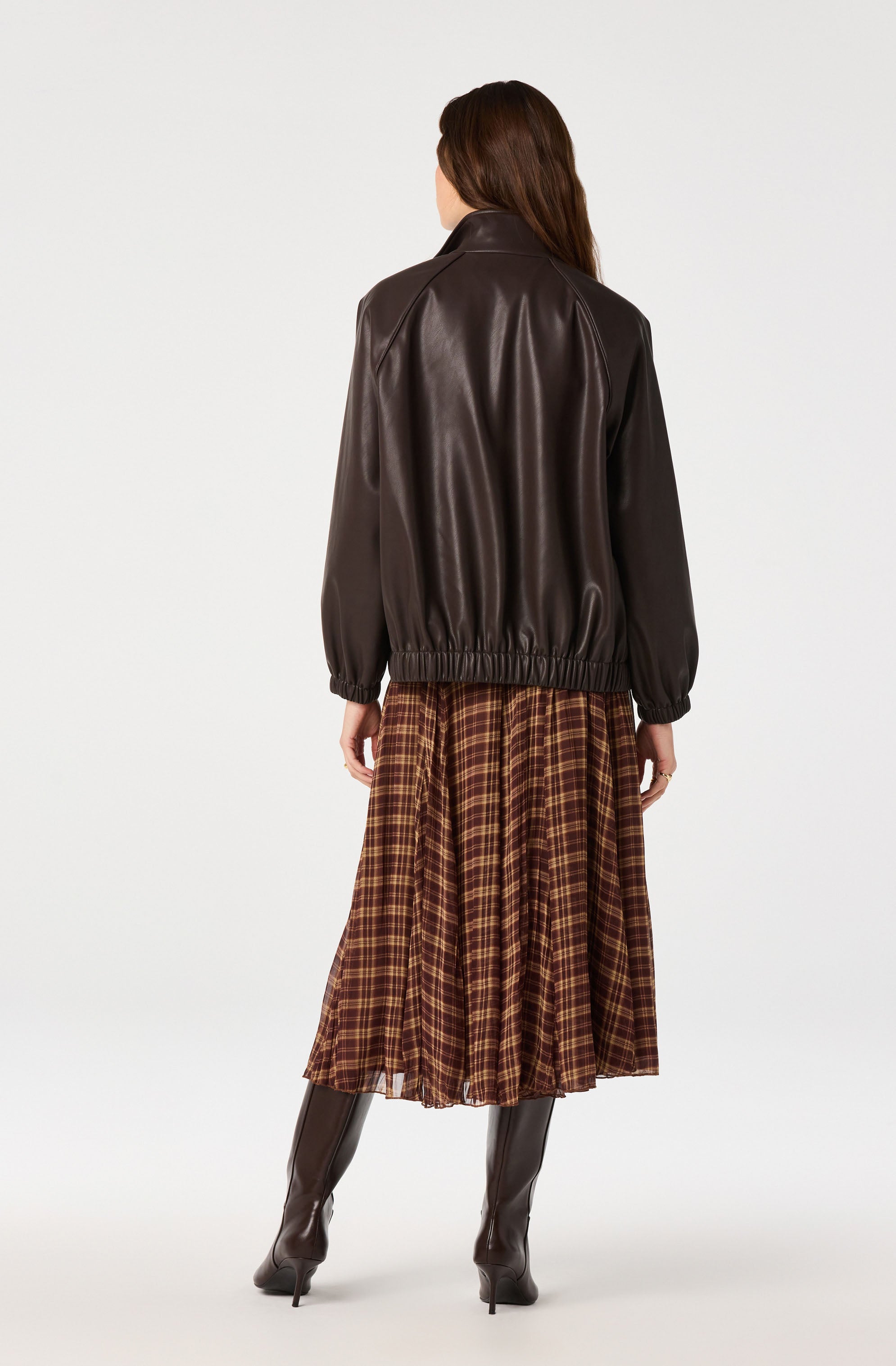 Woman wearing a dark brown leather jacket, plaid skirt, and black knee-high boots.