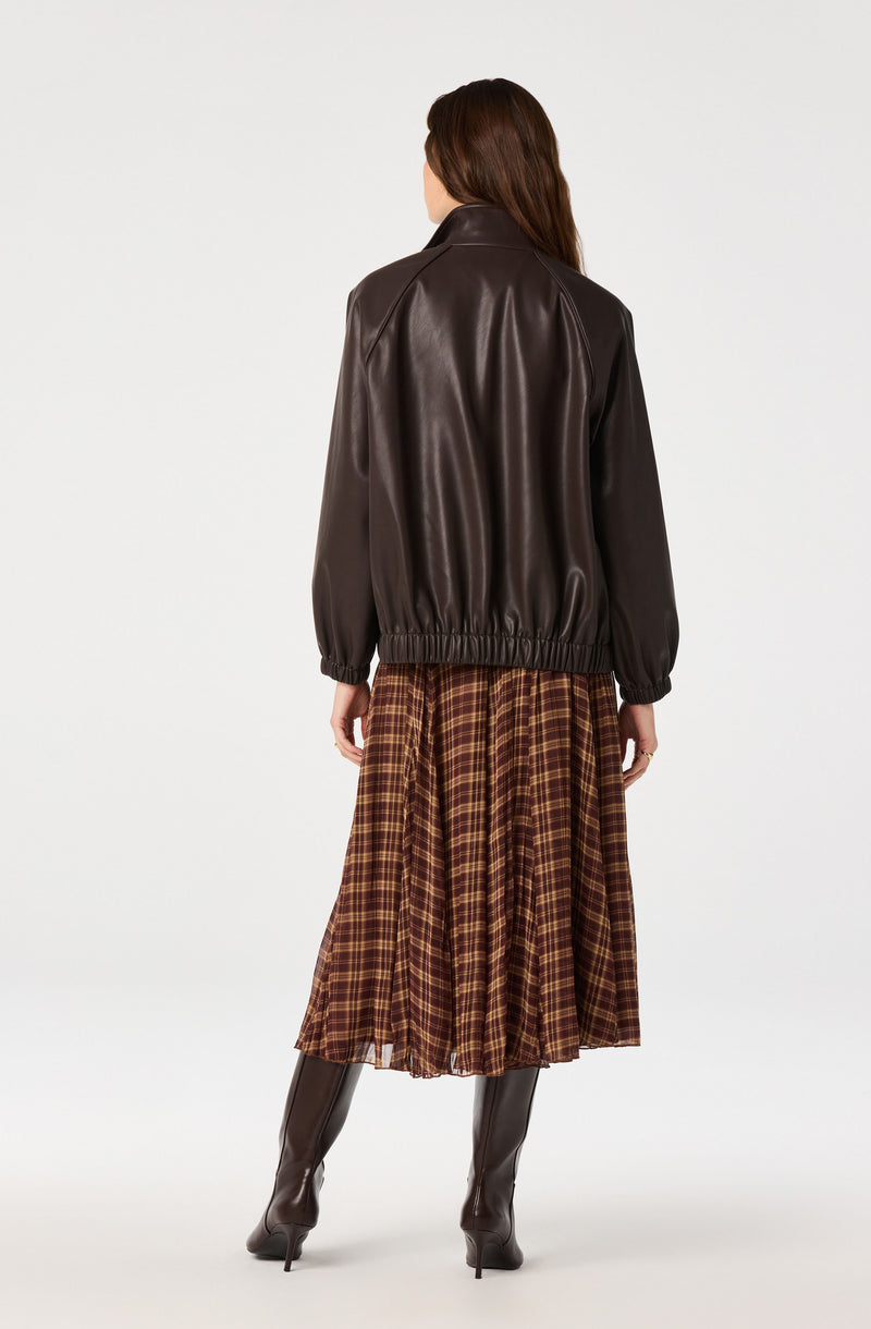 Woman wearing a dark brown leather jacket, plaid skirt, and black knee-high boots.