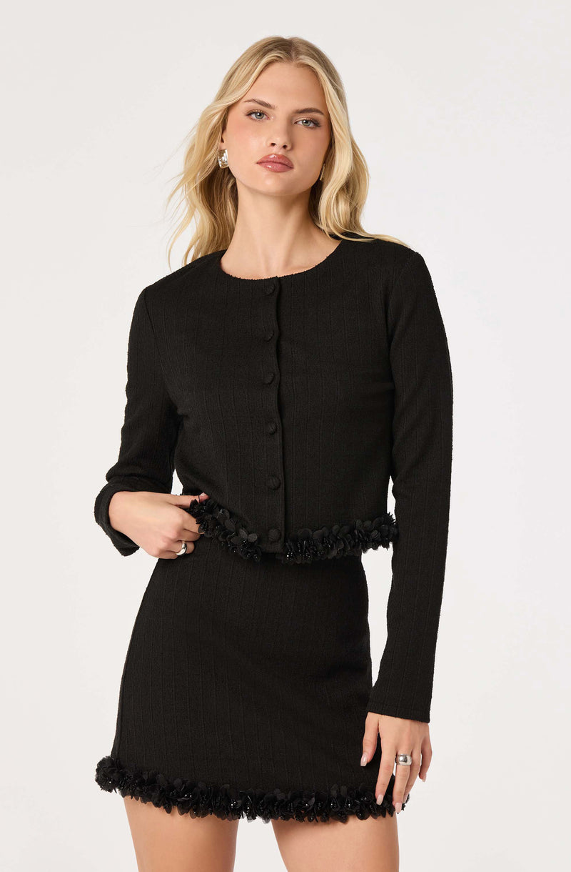 Woman wearing a black long-sleeve top and matching black skirt with textured edges.