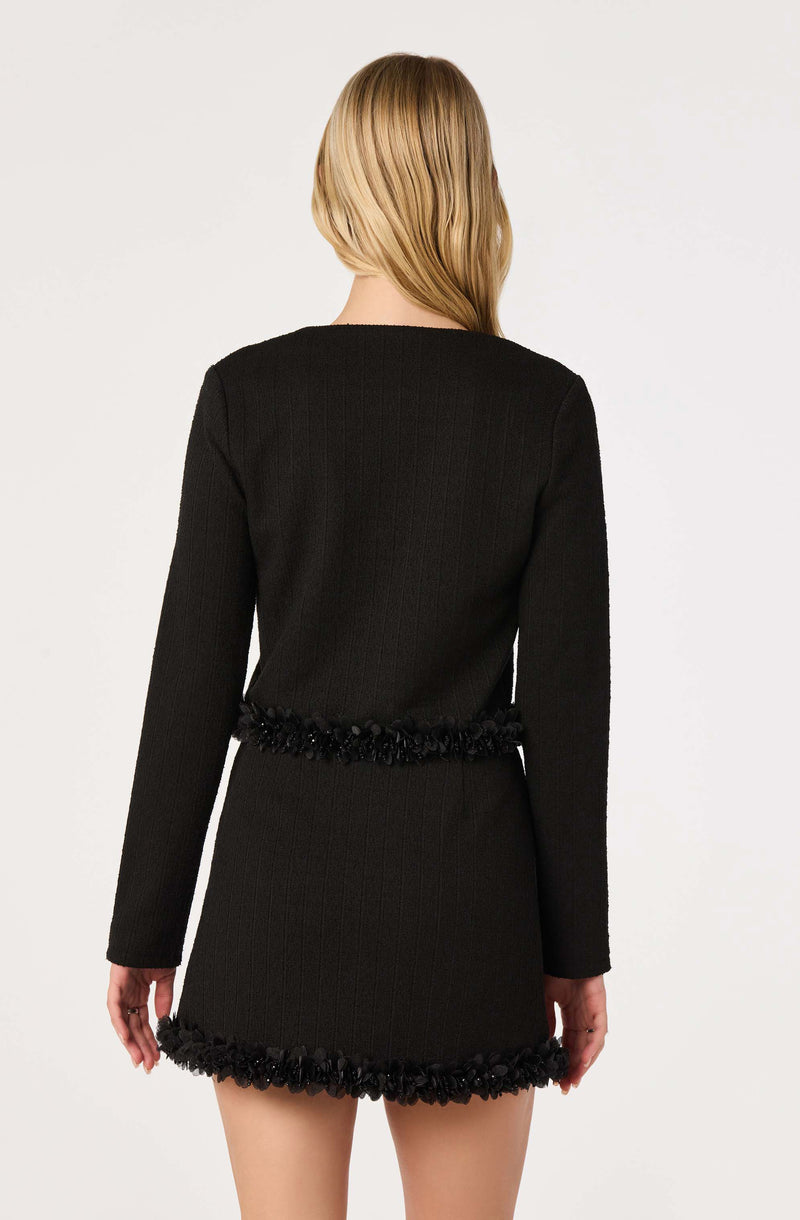 Black knit dress with textured trim and decorative fringe at hem and waist.