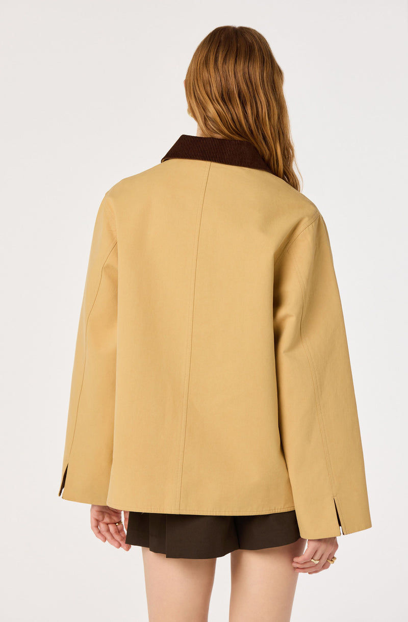 Woman in a beige jacket with a dark brown collar and dark shorts, seen from the back.