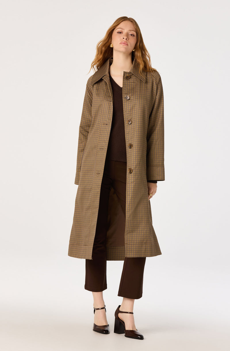 Woman wearing a long plaid coat, brown pants, black top, and black heels.