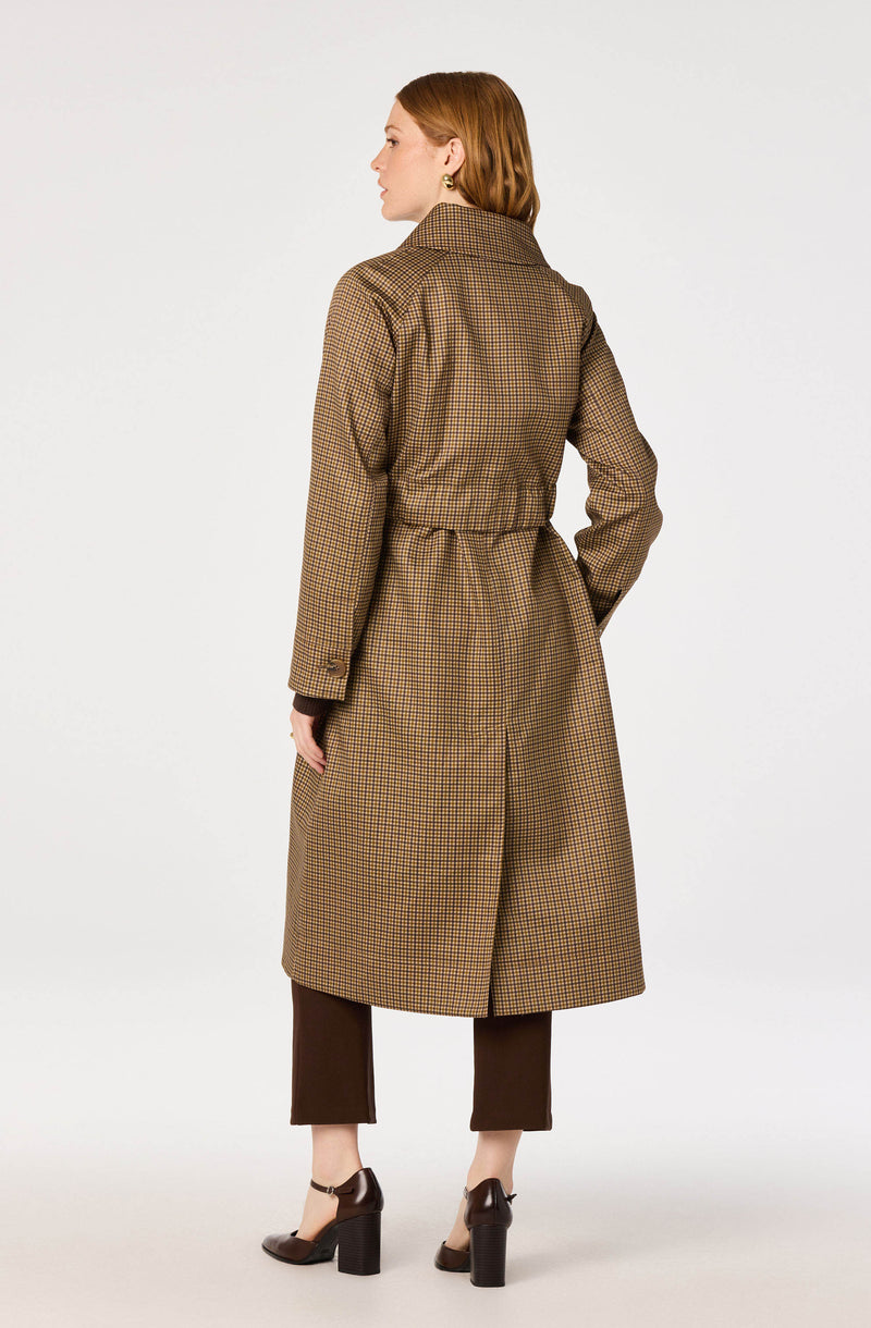 Woman wearing a long, brown checkered trench coat with matching belt, dark pants, and high heels.