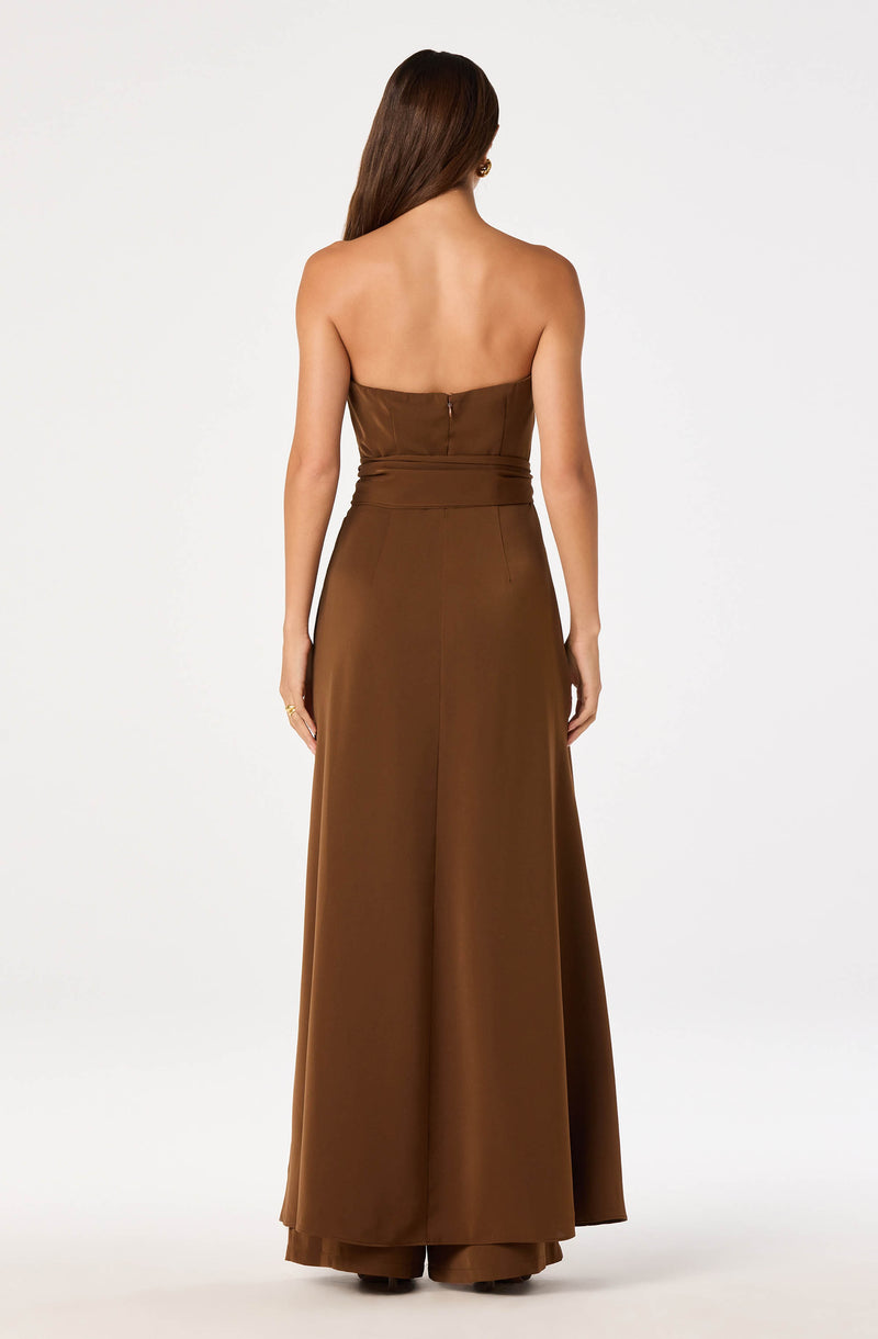 Back view of a woman in a strapless, brown, wide-leg jumpsuit with a fitted waist.