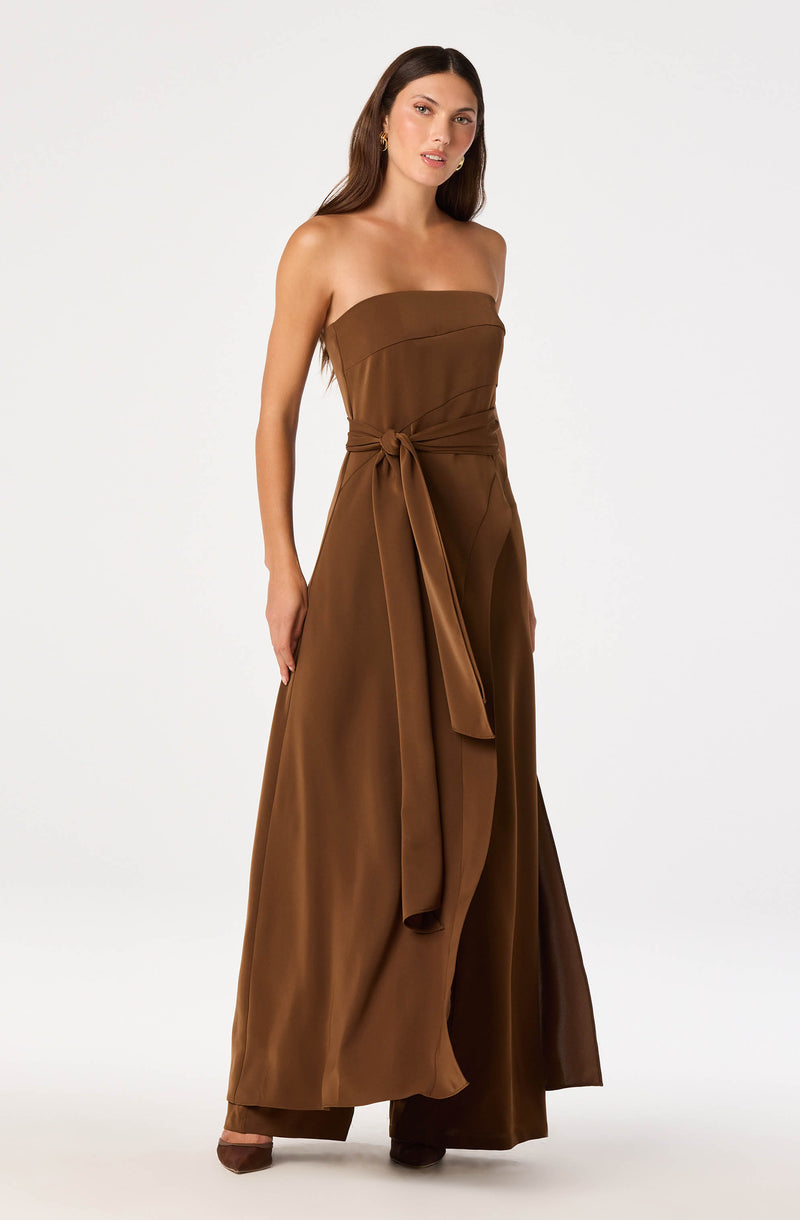 Brown strapless jumpsuit with a wide sash tied at the waist and wide-leg pants.