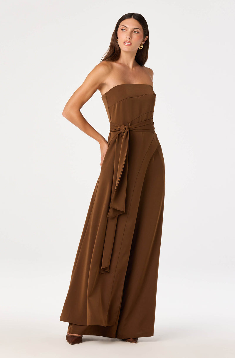 Woman in brown strapless jumpsuit with wide-leg pants and a tied sash at the waist.