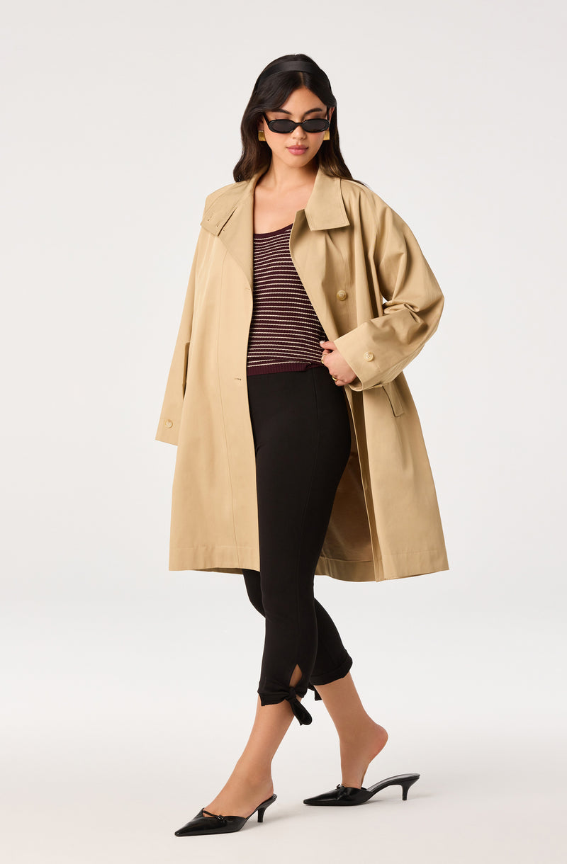 Woman in black tights, beige trench coat, striped top, black high heels, and sunglasses.