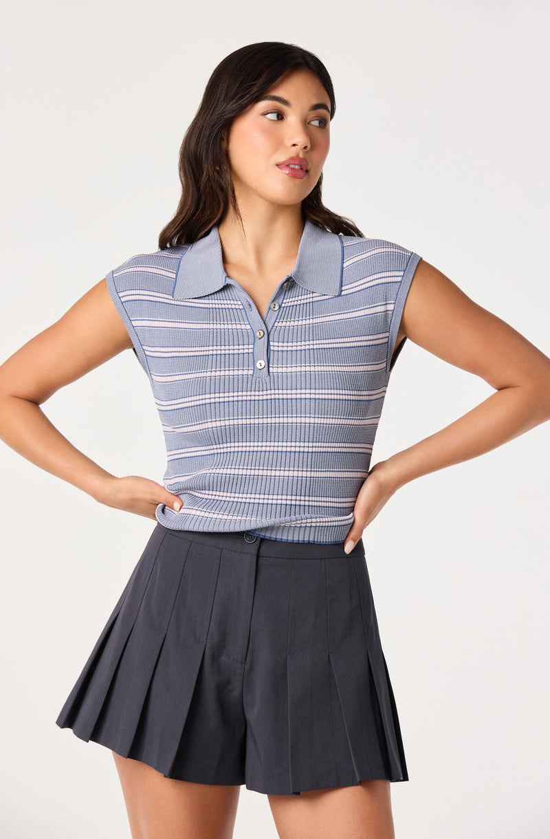 Woman wearing a blue striped sleeveless polo shirt and black pleated shorts.