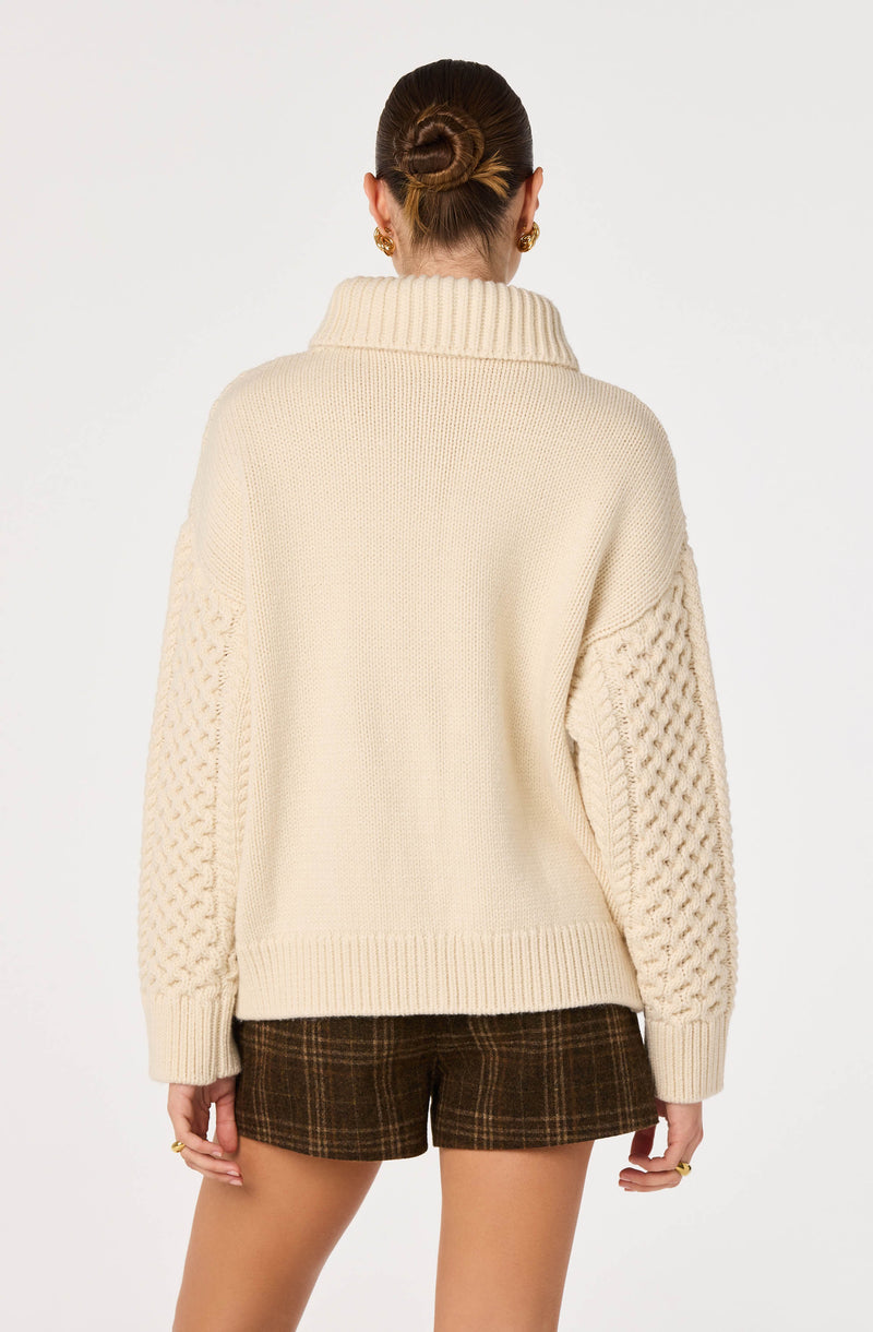 Cream chunky knit sweater with textured sleeves and a thick turtleneck.