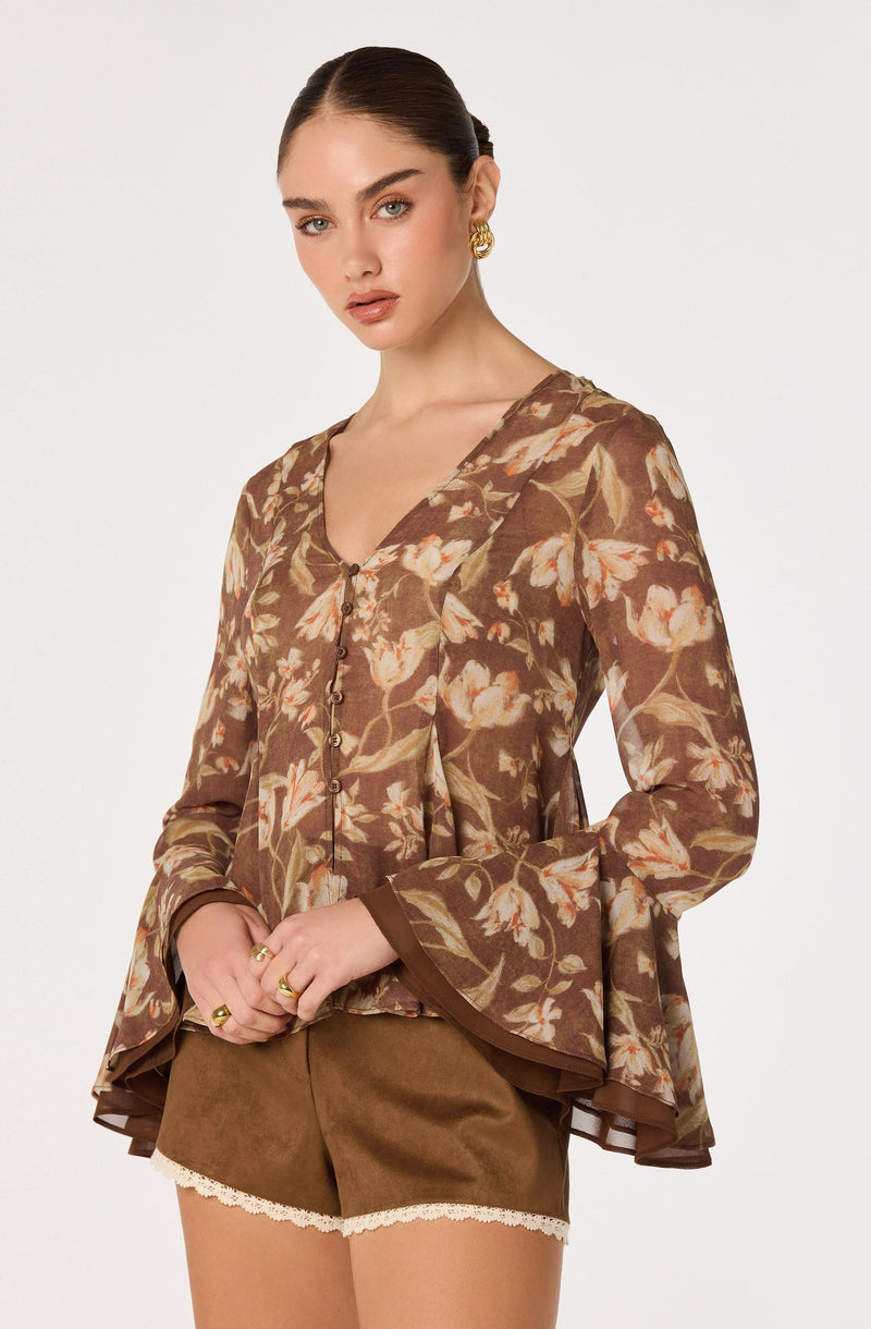 Woman wearing a floral brown blouse with bell sleeves and a V-neck, paired with brown shorts with lace trim.
