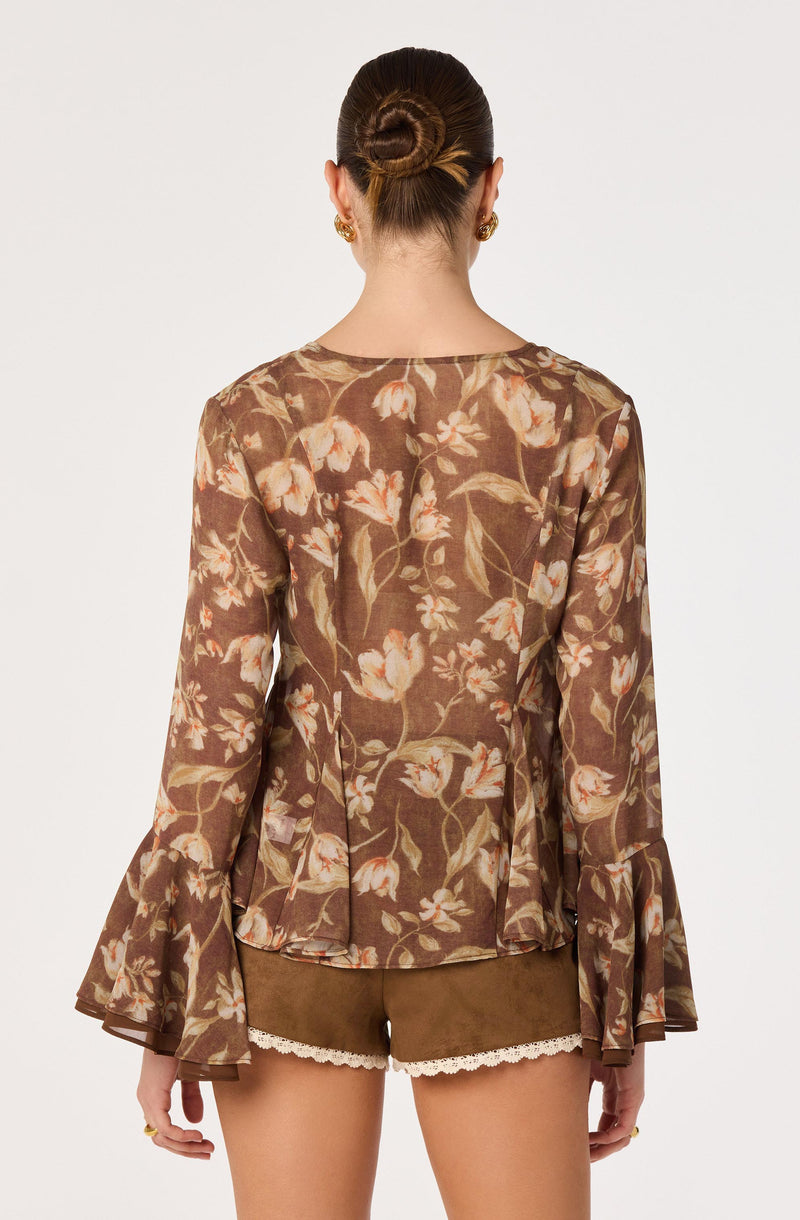 Woman wearing a floral long-sleeve blouse with ruffled cuffs and beige shorts with lace trim.