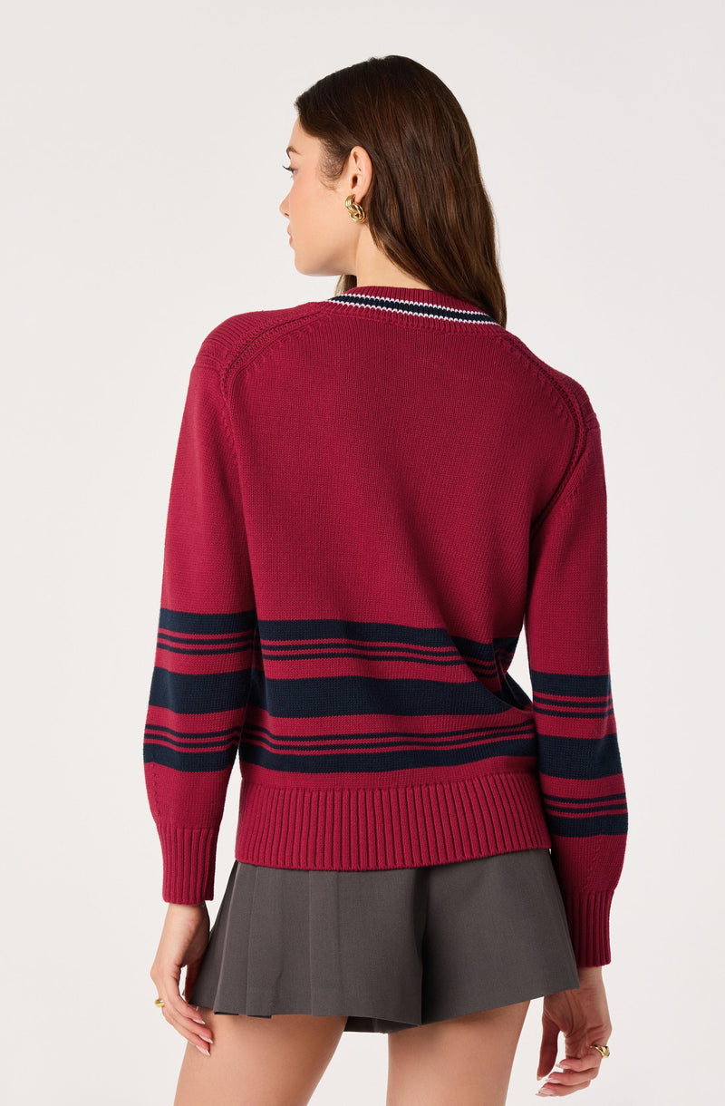 Woman wearing a red sweater with navy blue and red stripes, paired with a gray pleated skirt.