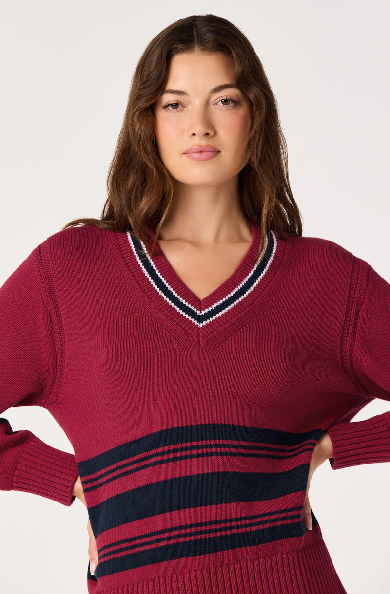 Woman wearing a red sweater with navy and white striped accents on the V-neck collar and hem.