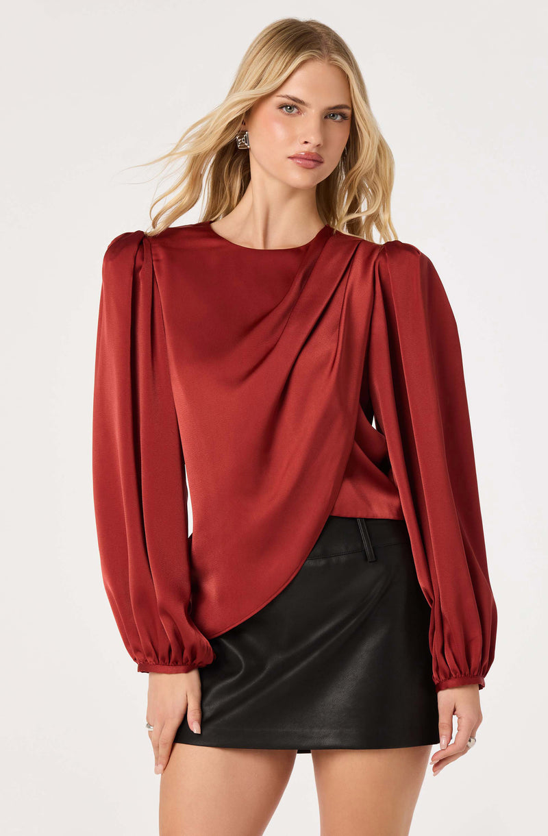 Woman wearing a red satin long-sleeve blouse with puff shoulders and a black leather mini skirt.