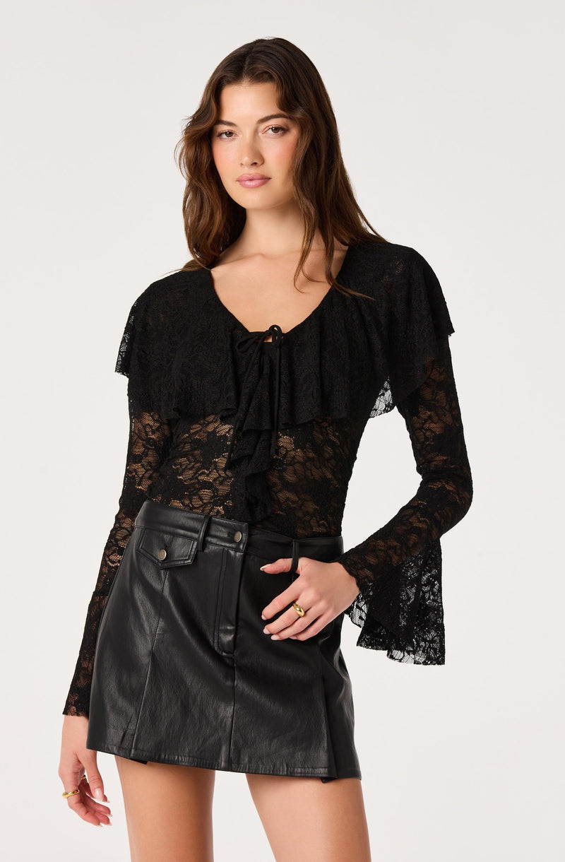 Woman wearing a black lace top with ruffles and bow detail, paired with a black leather mini skirt.