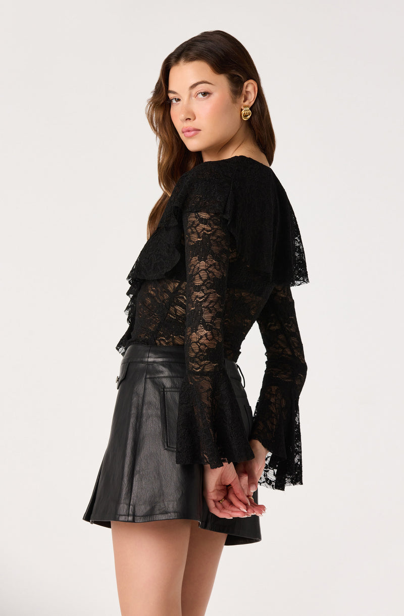 Woman wearing a black lace long-sleeve top with ruffle details and a black leather skirt.