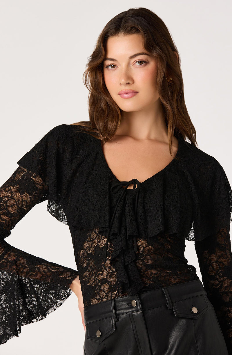 Woman wearing a black lace top with ruffles and bell sleeves.