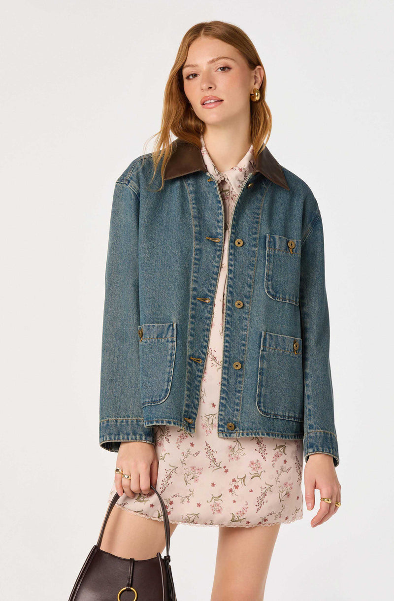 Woman wearing a blue denim jacket with a dark collar and a floral dress.