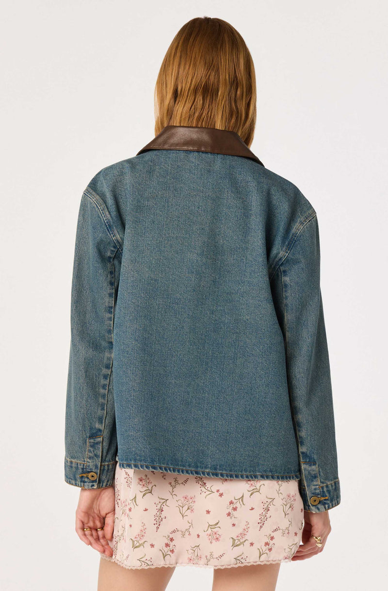 Woman wearing a denim jacket with a brown leather collar and a floral skirt.