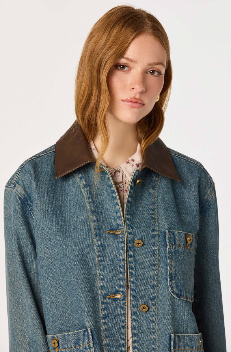 Woman wearing a blue denim jacket with brown leather collar and dark stitching.