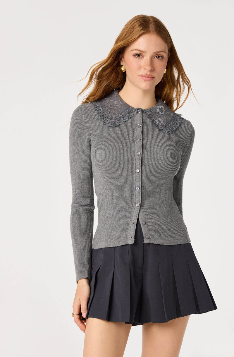 Woman wearing a gray ribbed knit cardigan with a lace collar and pearl buttons, paired with a dark pleated skirt.