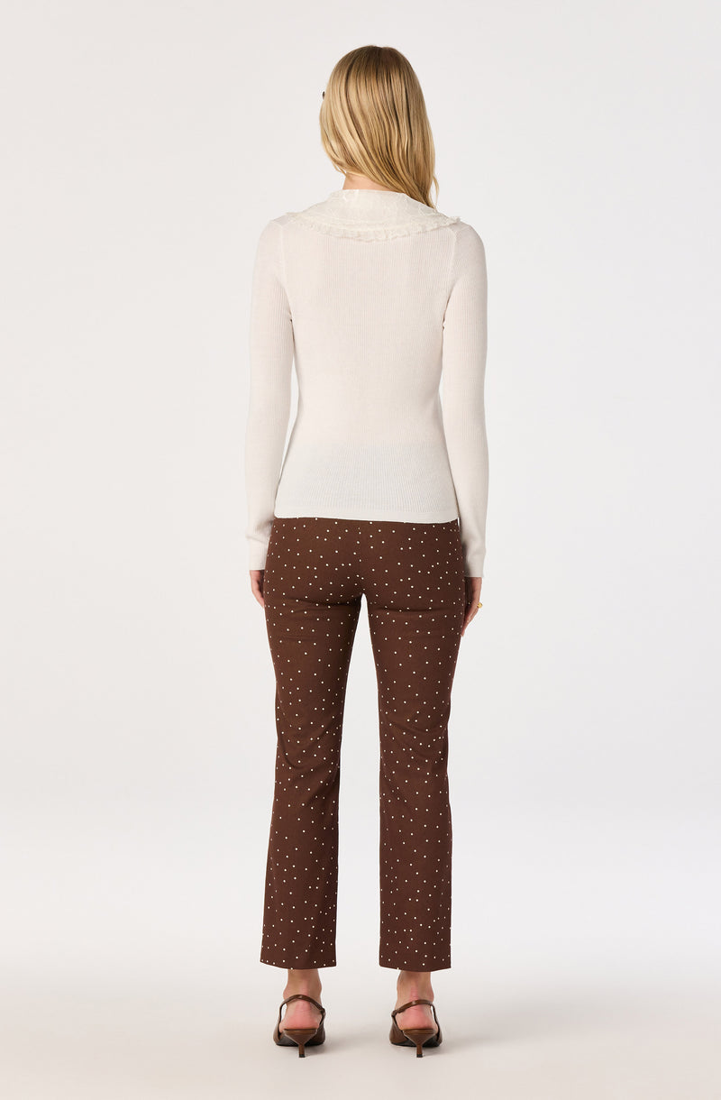 Woman wearing a white long-sleeve sweater and brown pants with white polka dots, high heels.