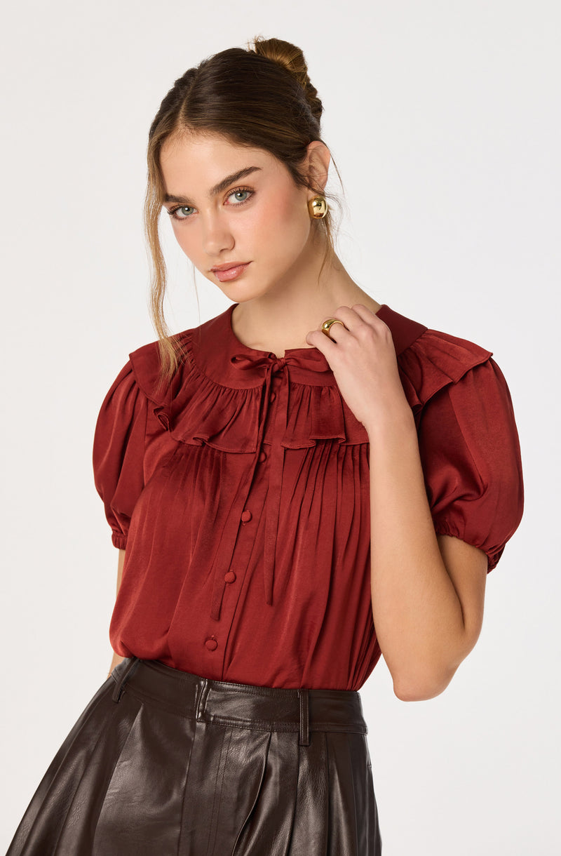 Woman wearing a dark red satin blouse with ruffle details and short puffed sleeves.