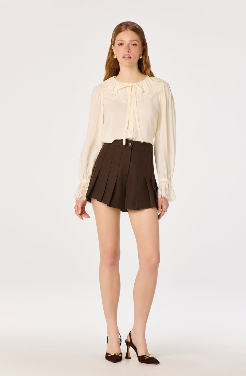 Cream blouse with lace details and long puffed sleeves paired with dark pleated shorts.