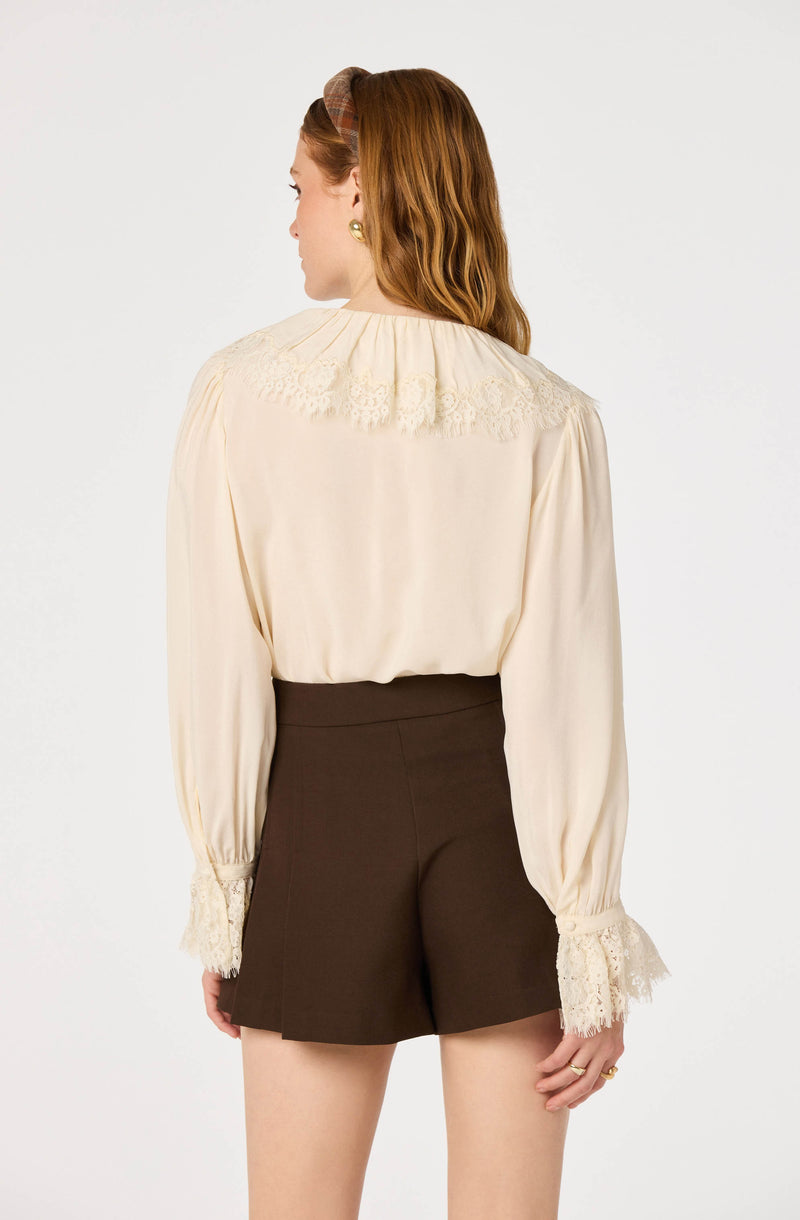 Woman in cream blouse with lace details on shoulders and cuffs, paired with high-waisted dark shorts.