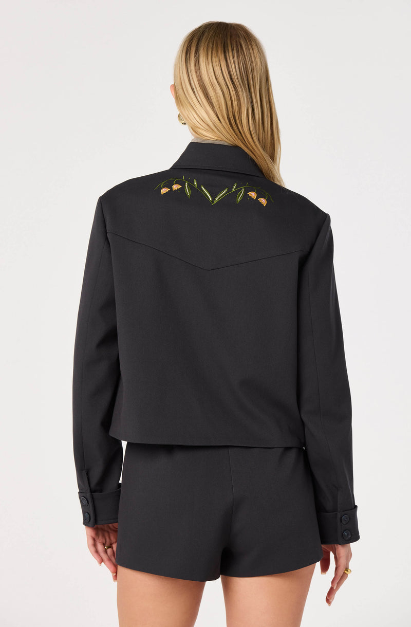 Black cropped jacket with floral embroidery on the back, paired with matching black shorts.