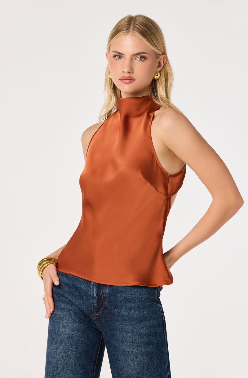 Woman wearing a sleeveless, shiny bronze satin top and blue jeans.