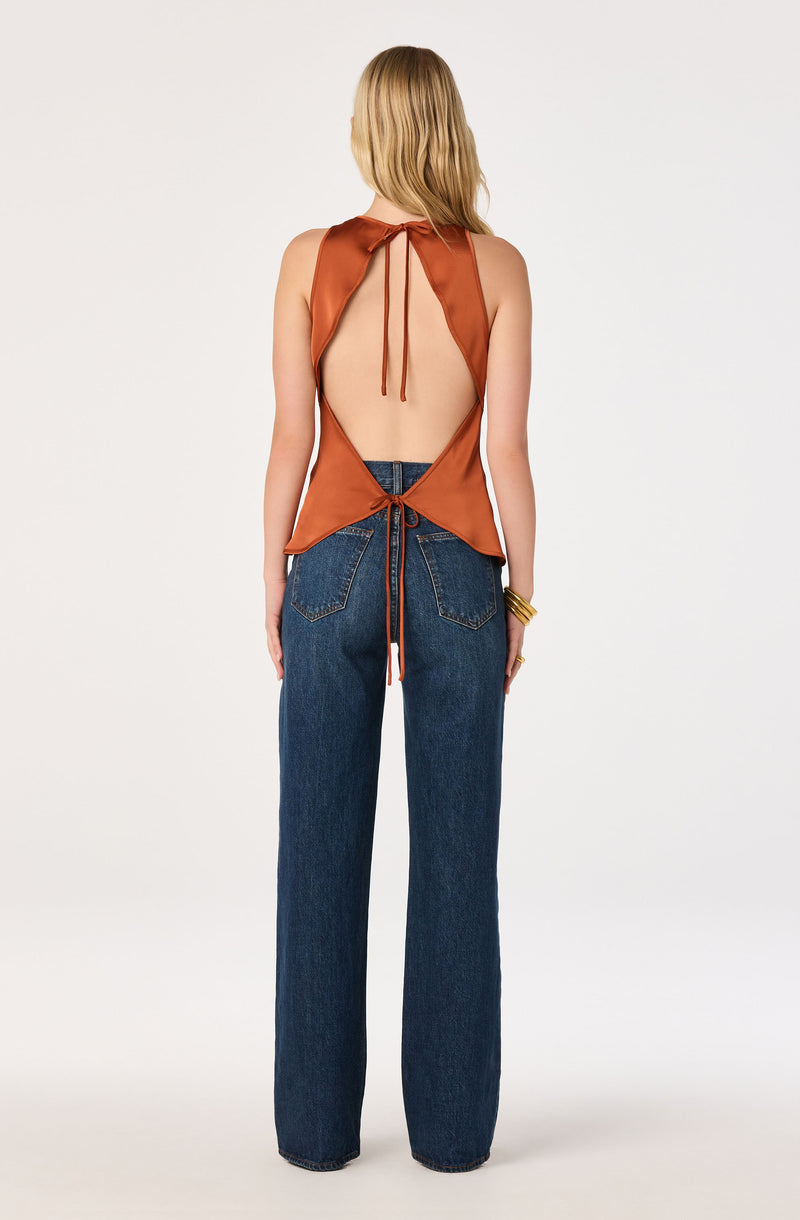 Back view of a woman wearing a sleeveless, open-back satin top in rust color with ties, paired with high-waisted, straight-leg blue jeans.