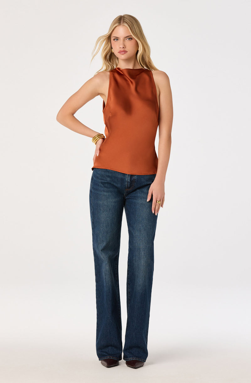 Woman wearing a shiny, sleeveless, rust-colored satin top and blue jeans.
