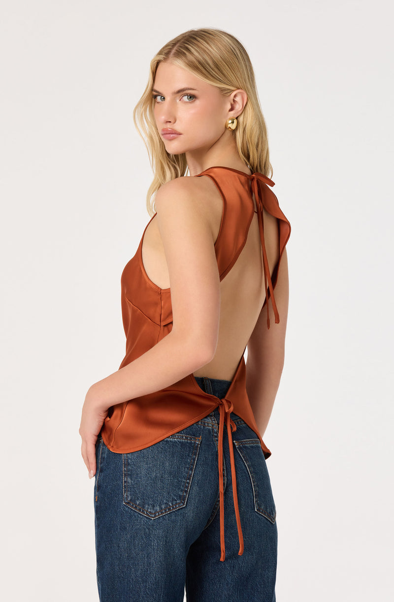 Girl with blonde hair in a rust-colored sleeveless top with open back and tied straps, paired with blue jeans.