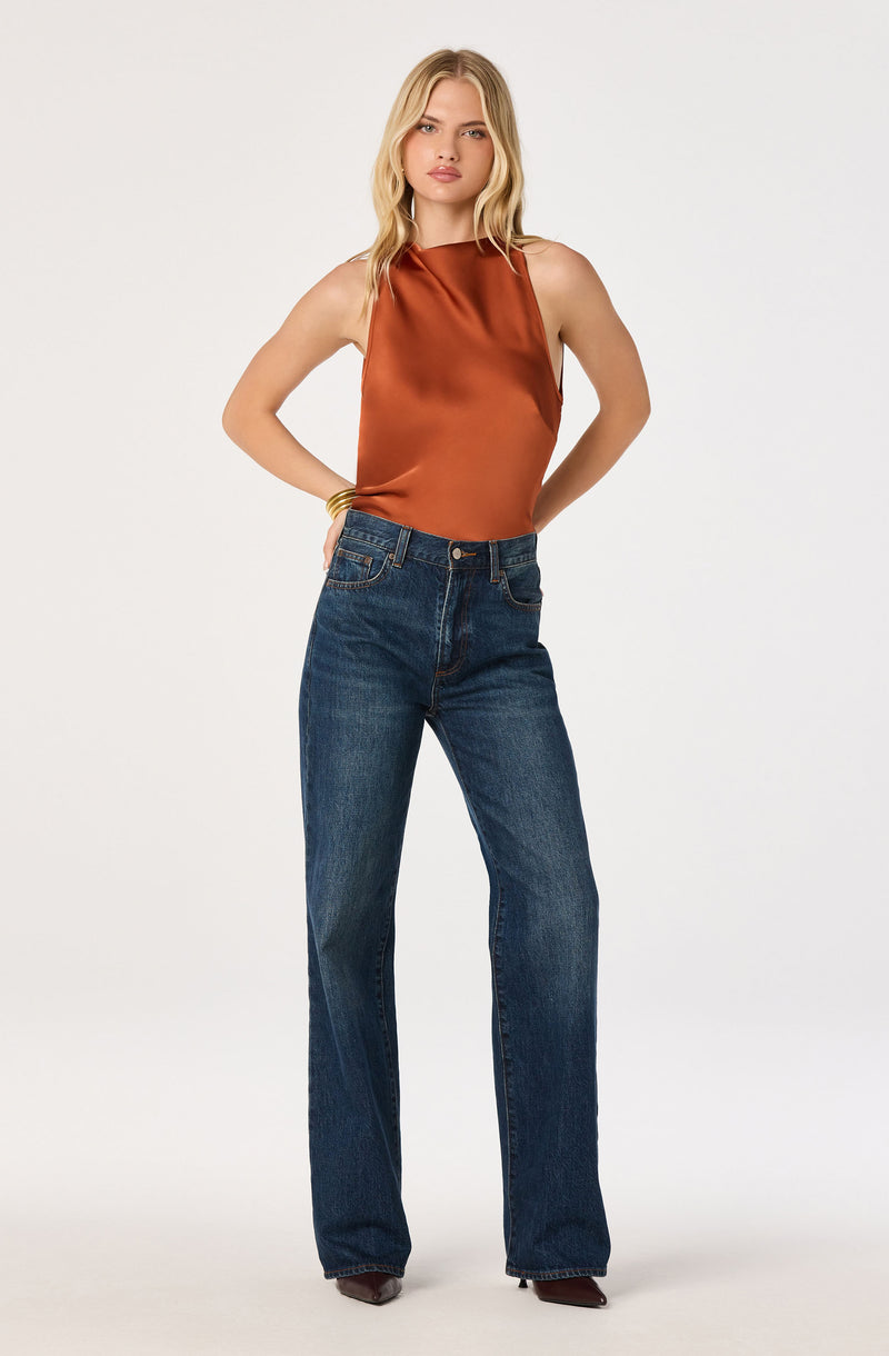Woman wearing a shiny, brown sleeveless satin top and high-waisted blue jeans.