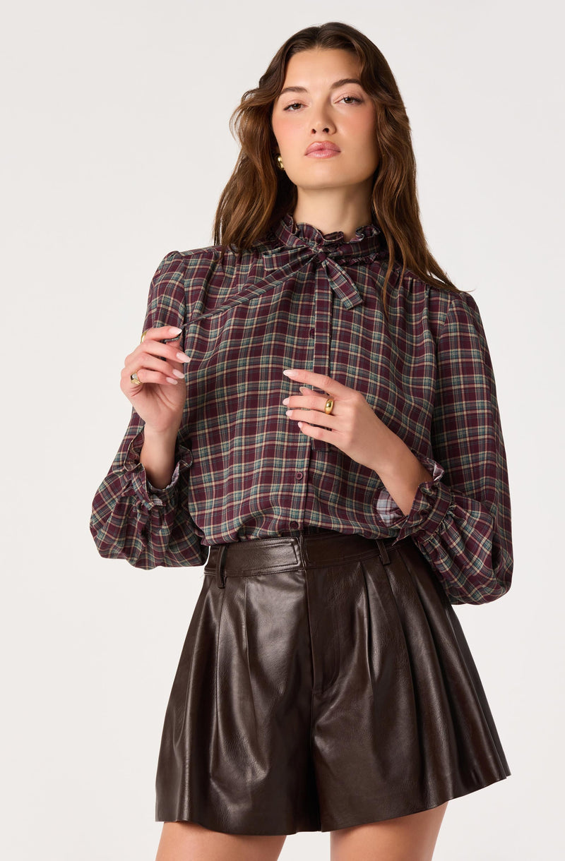 Woman wearing a plaid blouse with ruffled collar and high-waisted leather shorts.