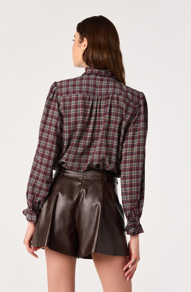 Woman wearing a plaid long-sleeve shirt and high-waisted brown leather shorts.